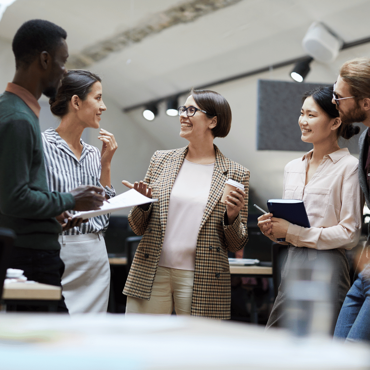 A group of diverse colleagues standing in a modern office space, smiling and talking together during a meeting.